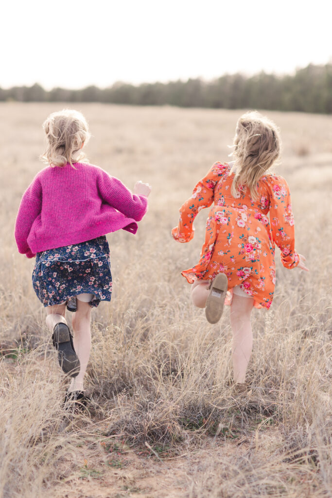 Girls running through a field in floral dresses during their fall family portraits