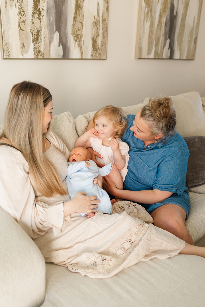 Family cuddling together on couch during relaxed postpartum photography session.