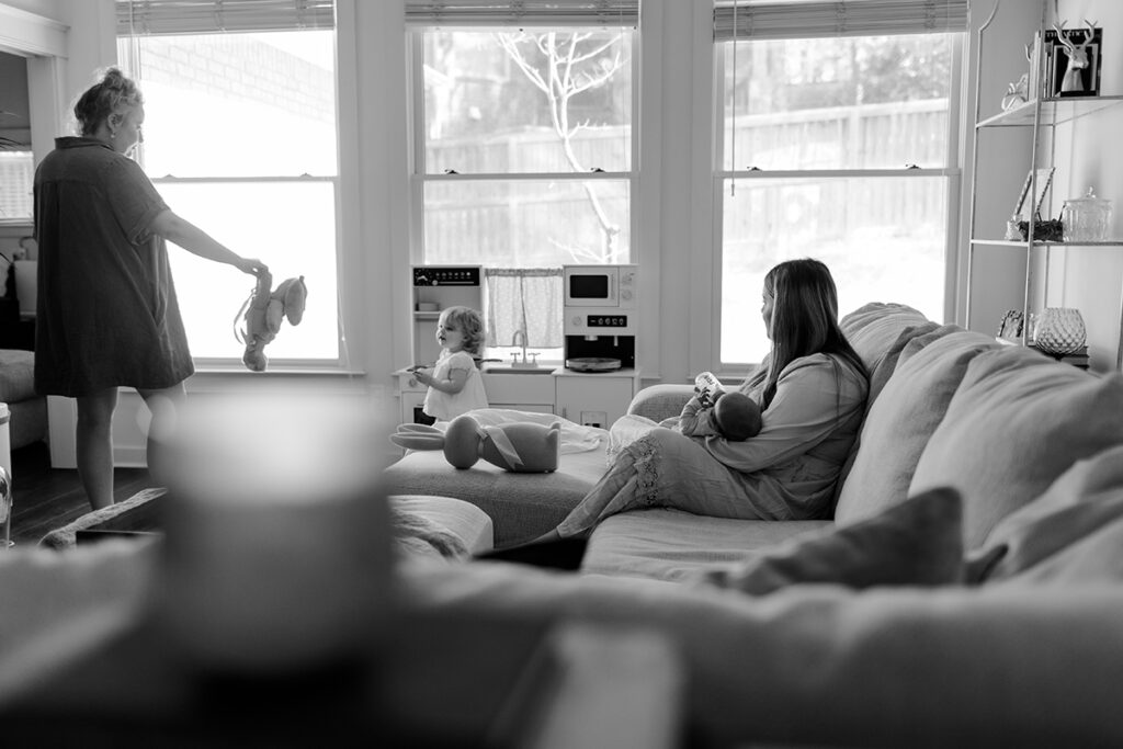 Black and white lifestyle photo capturing a quiet moment between two mothers and their children.
