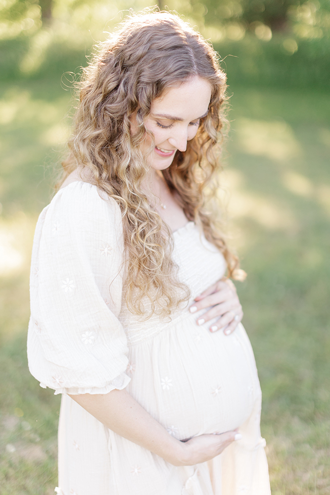 Pregnant woman in a flowing dress laughing in a Little Rock during golden hour.