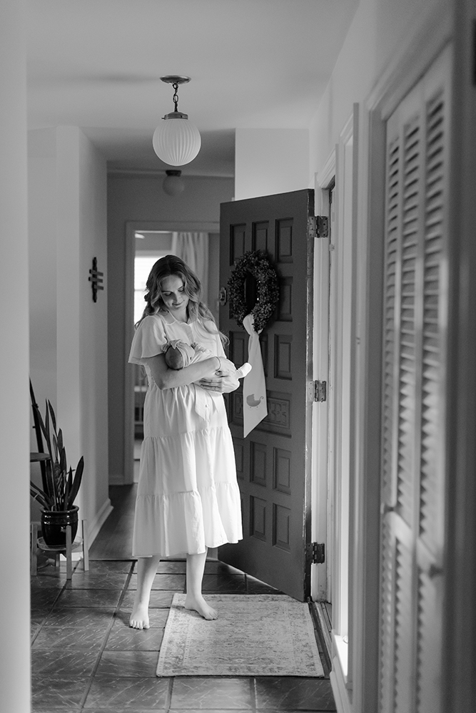 mother holding her newborn in a hallway in their home