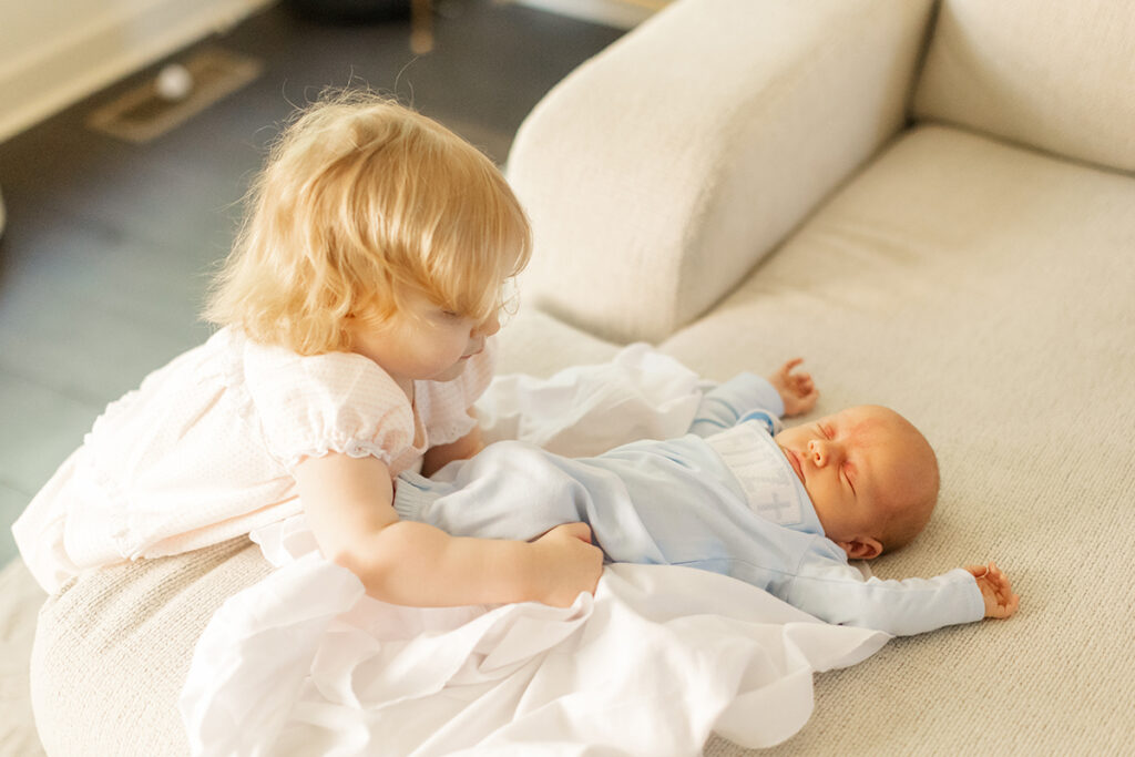 Toddler cuddling newborn baby brother during candid sibling moment.