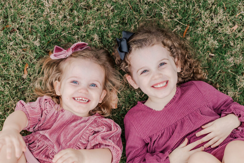 Sisters in rich berry-toned dresses smiling on fall grass during a cozy Arkansas family photo session