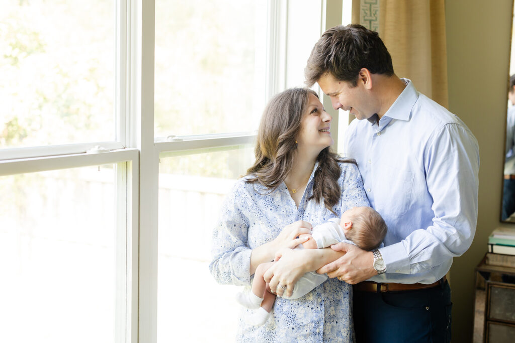 mom and dad holding newborn by the window light